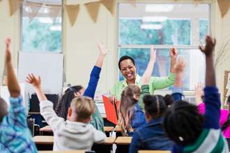 teacher in classroom with students all raising their hands