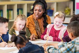 teacher kneeling down to students level and helping with work in her classroom