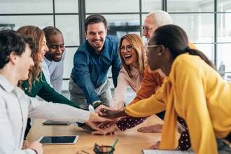 team of smiling coworkers putting their hands together for a cheer