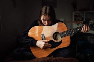 teenage girl looking sad while playing the guitar