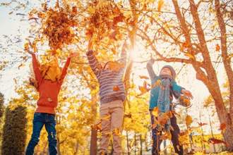 three children jumping in the air throwing fall leaves in the air