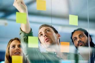three coworkers looking at a board while jotting down notes for an upcoming projects