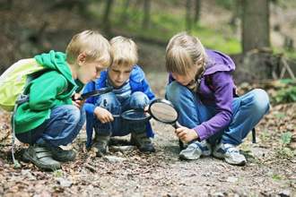 three kids looking at the ground with magnifying glasses