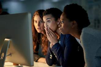 three women looking shocked and confused at a computer screen