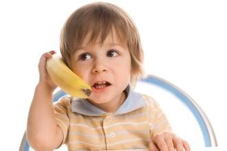 toddler sitting in a high chair talking into a banana like a cell phone