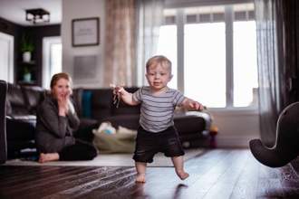 toddler taking small steps while his mother looks on