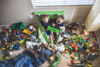 two boys sitting in a messy room surrounded by their toys