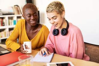 two friends sitting at a table together looking over one persons work