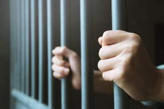 two hands tightly wrapped around their jail cell bars