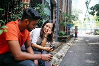 two individuals sitting on the sidewalk talking to each other with smiles on their faces