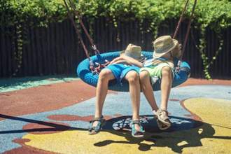 two kids laying on a swing in the sun with hats covering their faces