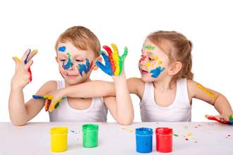 two kids sitting at the table using finger paint to paint on their bodies