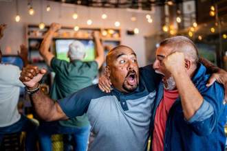 two men looking excited at one another after their favorite team scored a goal