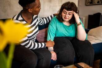 two people sitting on a couch with one comforting the other who looks upset