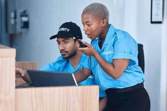two security guards looking at a computer screen making commands into a walkie talkie