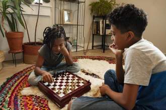 two siblings concentrating while playing a game of chess on the family room floor