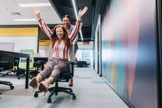 two women enjoying free time in the office playing around in their chairs