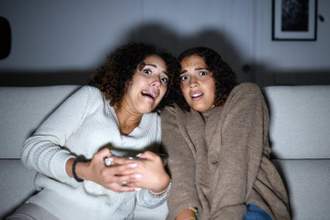 two women looking terrified on the couch while watching television