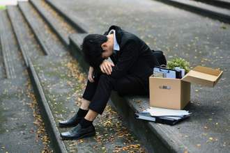 upset worker who was just fired sitting on steps with a box of their personal items next to them