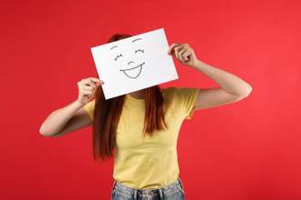 woman holding a smile drawn on a piece of paper in front of her face