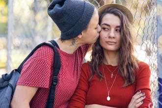 woman kissing her partner apologizing while they look annoyed