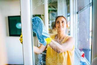 woman looking up at a large window that she is cleaning with a cloth