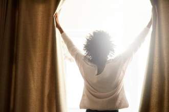 woman pushing curtains open while bright light streams into the room behind her