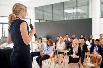 woman standing up on stage presenting to crowd in an office setting