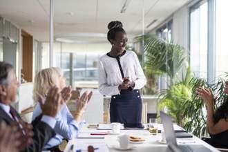 woman standing while her coworkers clap for her