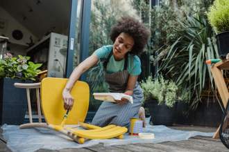 woman taking time to repaint a chair yellow in her backyard