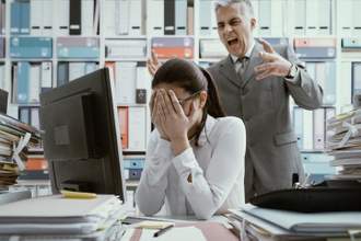woman with her head in her hands while her boss is yelling at her from behind
