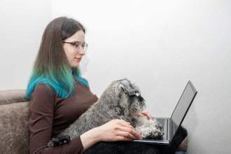 woman working on her computer while her dog sits in her lap and partially on her laptop