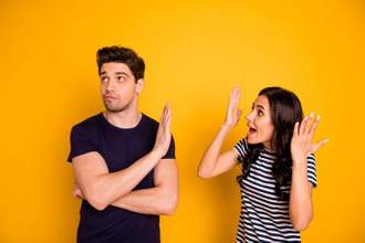 women looking frustrated trying to talk to her friend while he looks disinterested and holding a hand up to her face so she will stop talking