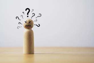 wooden figure looking distraught with question marks surrounding its head
