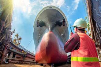 work man looking up at large cargo ship