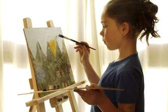 young child looking focuses while painting a landscape picture