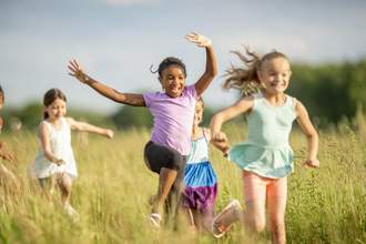 young children running excitedly through a grass field
