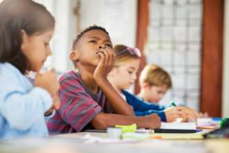 young student resting his face in his hand while looking thoughtfully up in the air
