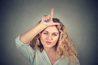 young woman looking rudely into the camera placing the loser sign on her forehead