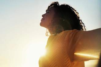 young woman with her arms outstretched and eyes closed while standing in the sunlight