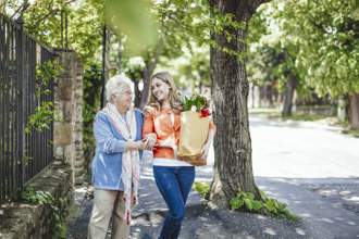younger woman helping an older lady with carrying her groceries to her home
