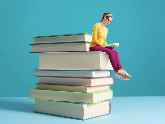tiny woman sitting on a pile of books reading